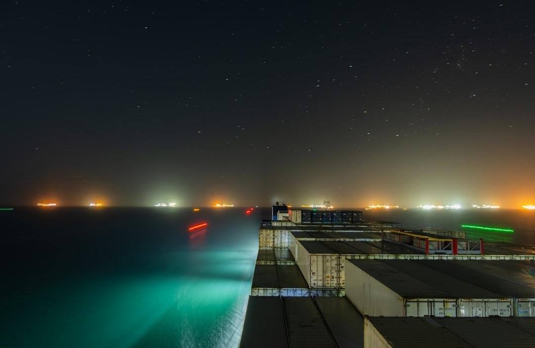 Cargo ship at sea with distant city lights at night.